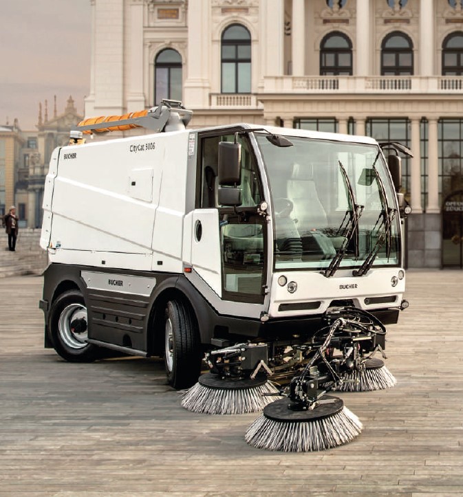 Bucher CityCat 5006 compact street sweeper with dual front brushes parked in front of a grand municipal building.