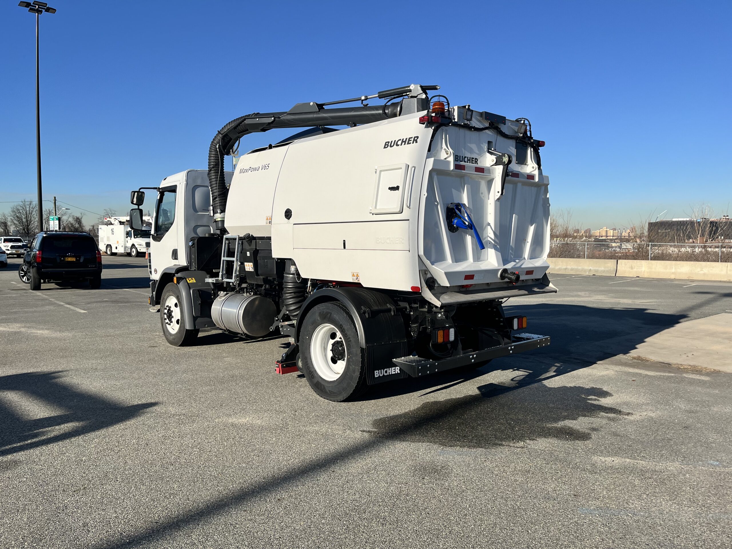 Rear-side view of a Bucher V65 GRV regenerative air street sweeper in a paved lot under a clear blue sky.